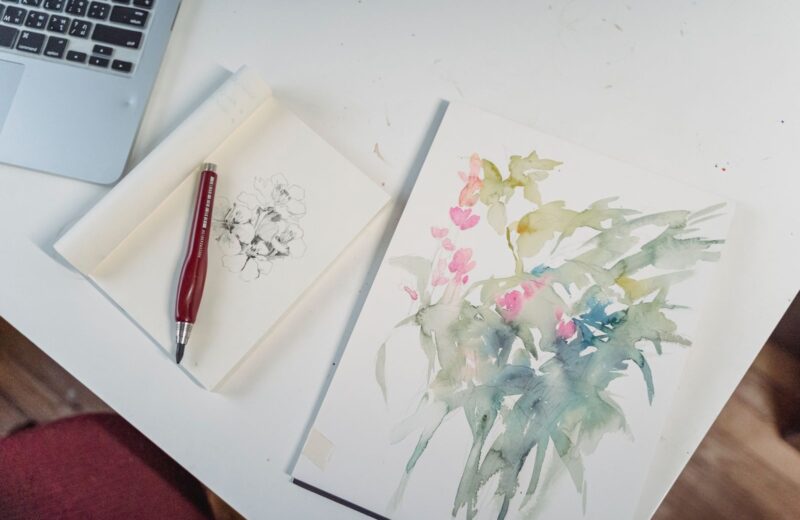 A pen beside a watercolour sketch of flowers on a white desk