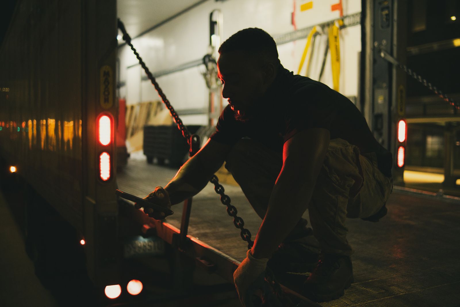 A driver tightening the chains on a truck's load at night