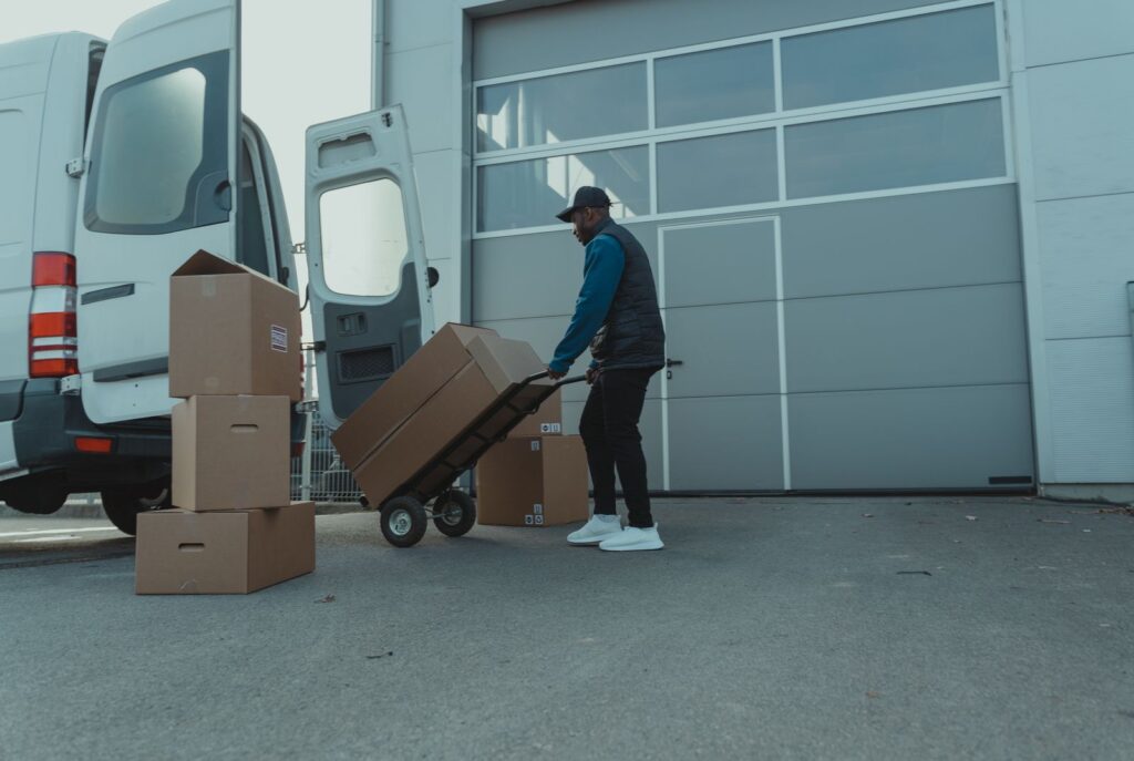 A courier wheeling boxes on a hand truck from a van to a warehouse door