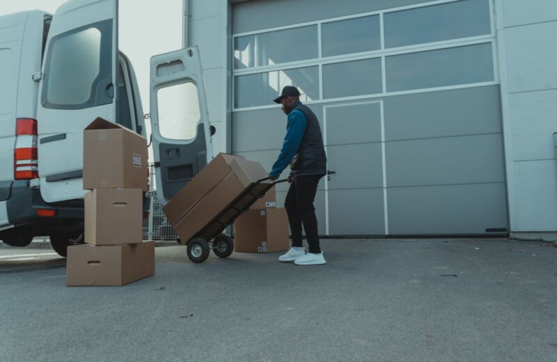 A courier wheeling boxes on a hand truck from a van to a warehouse door