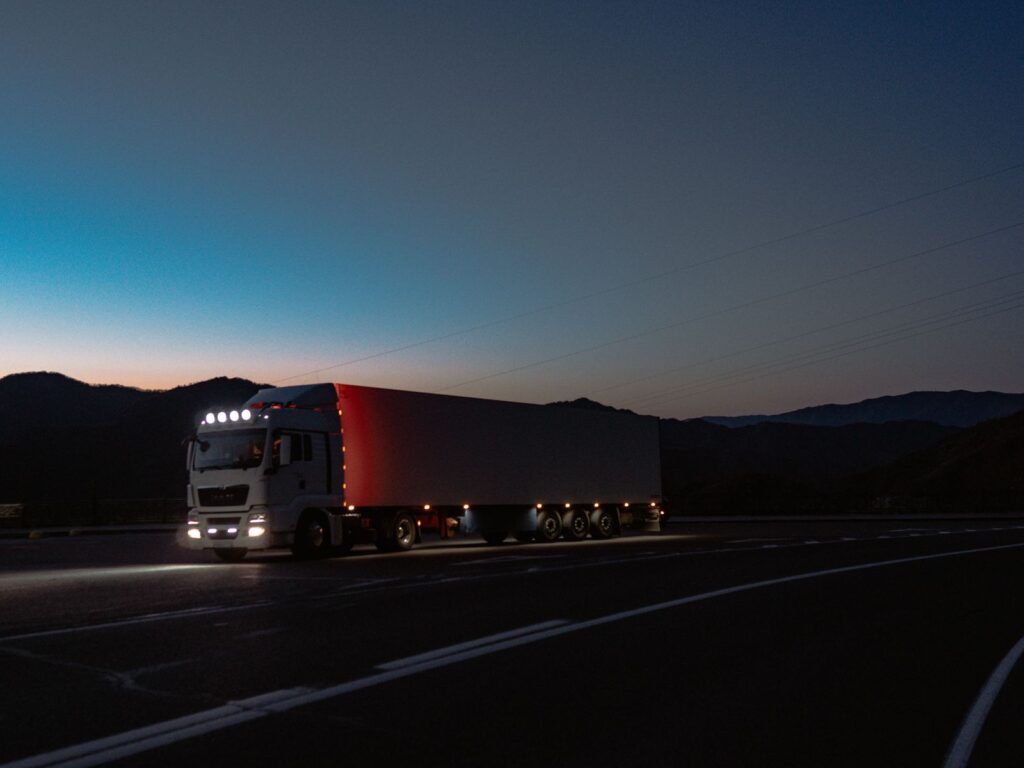 A truck with its lights on driving along a mountain road at dusk