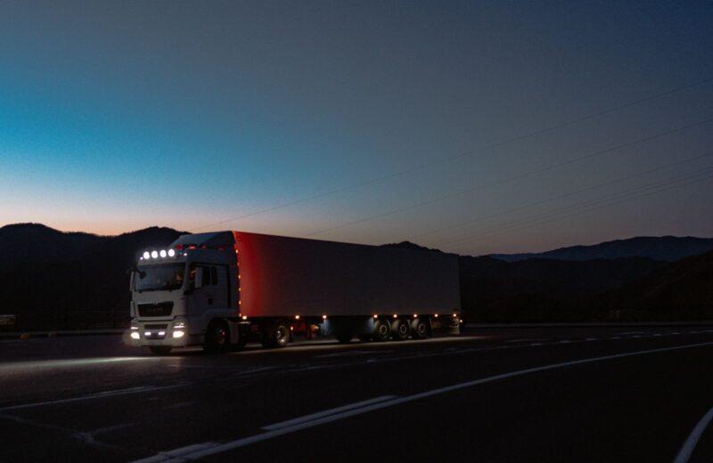 A truck with its lights on driving along a mountain road at dusk