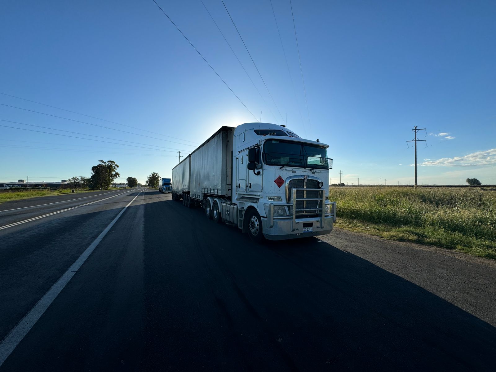 A road train driving towards the camera on an open highway at sunrise