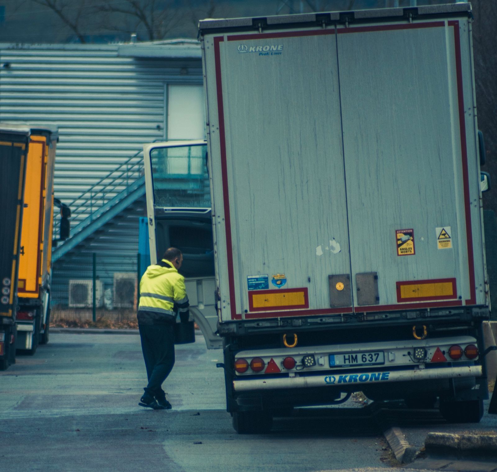 A worker in a high-visibility jacket at the rear doors of a trailer