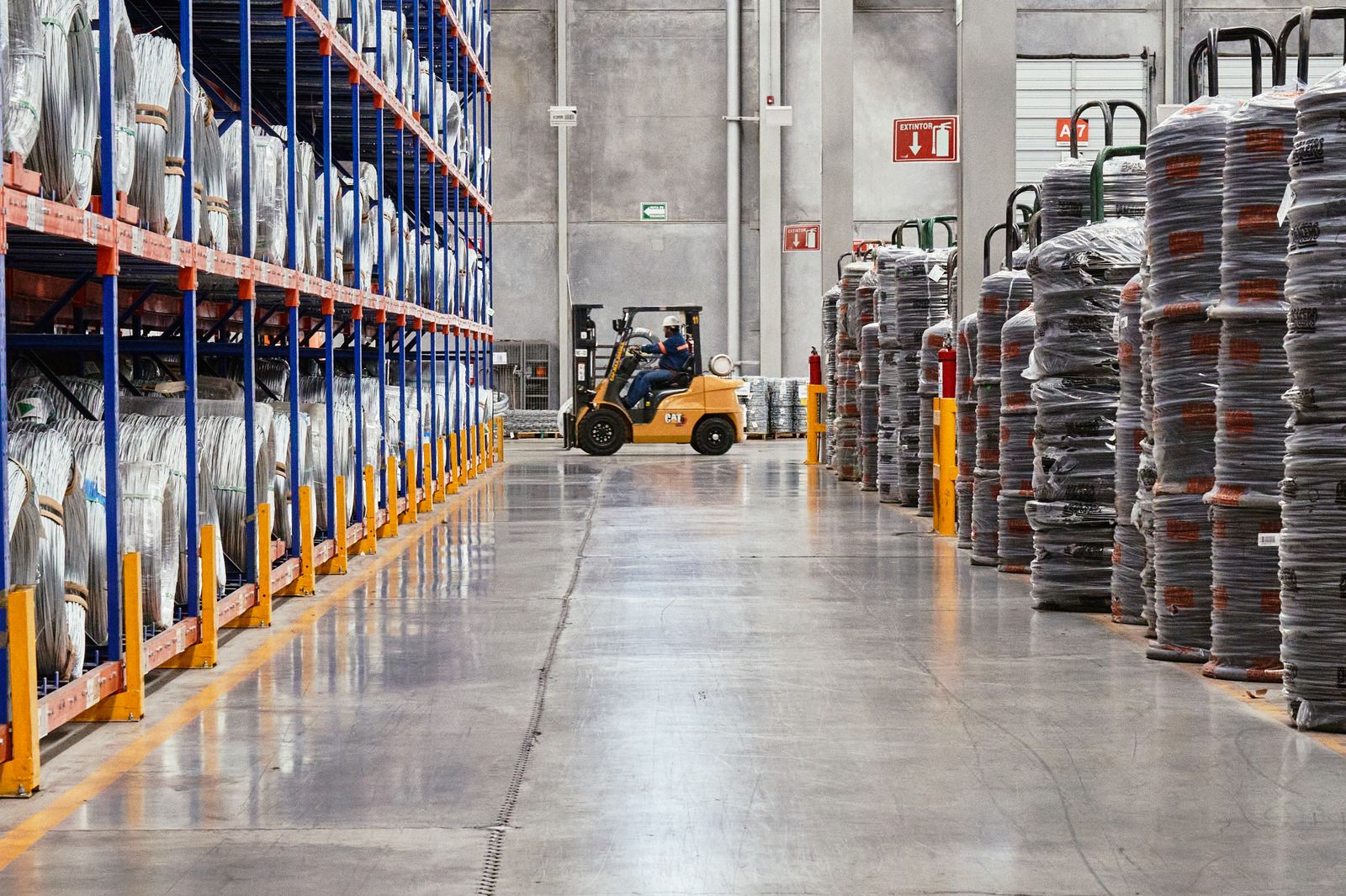 A forklift moving goods along a warehouse aisle between stacked loads
