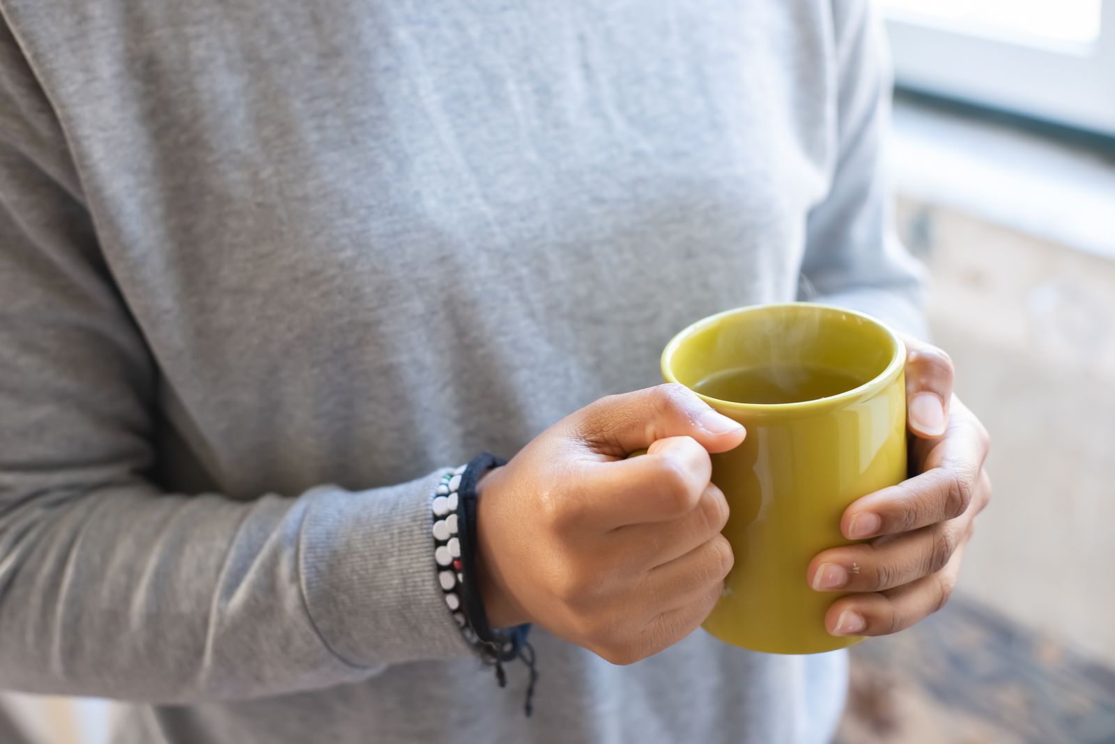 Hands in a grey sweater holding a mug of tea