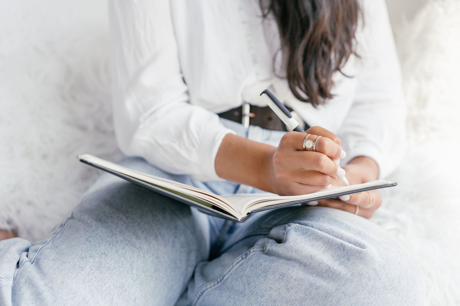 A person writing in a notebook on their lap, only hands and knees in view