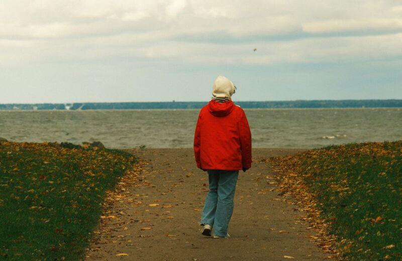 A person in a red jacket walking towards the sea on an autumn day