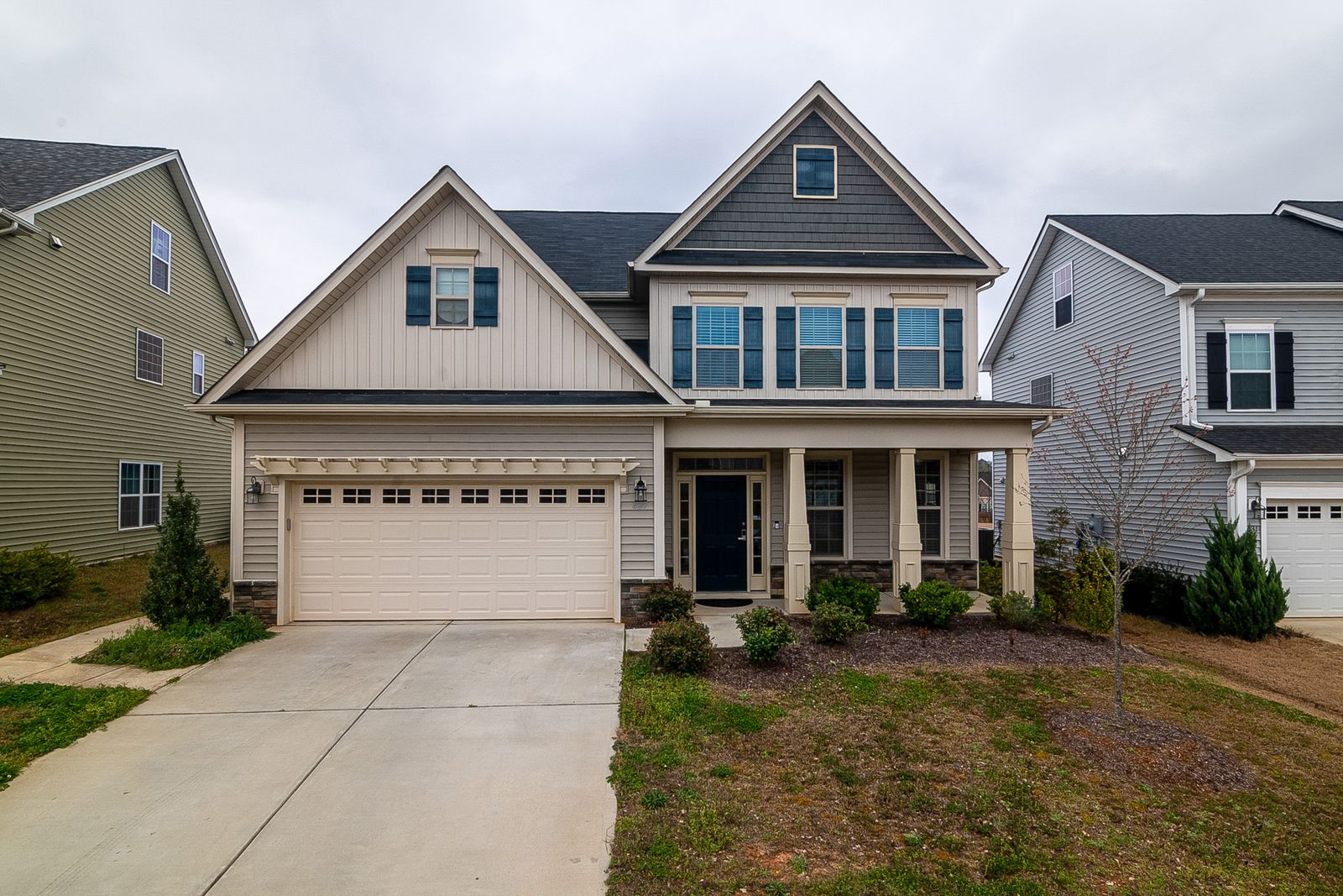 Two-storey family house with a front porch, a garage and young shrubs
