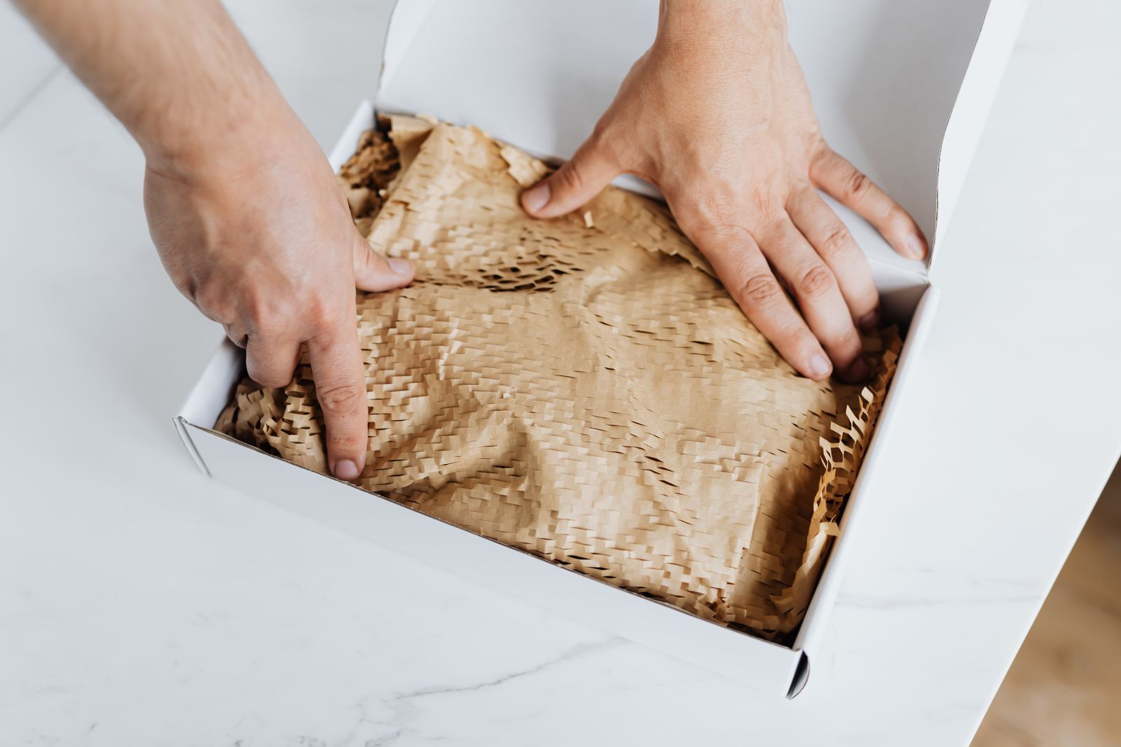 Hands pressing kraft paper padding into a white mailing box