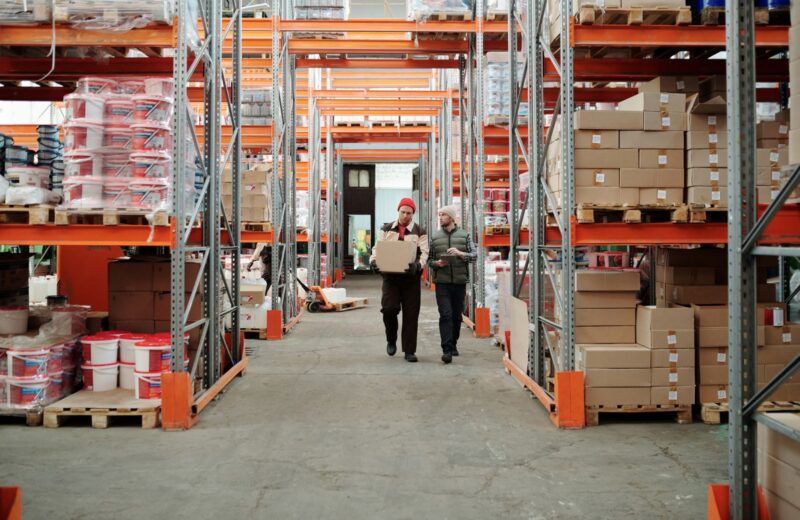 Two workers carrying a parcel along a warehouse aisle