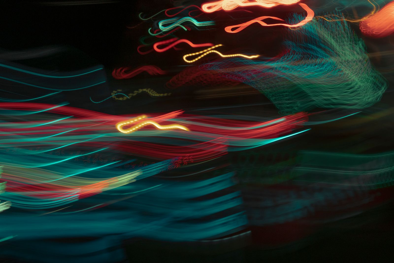 Colourful light trails in teal, red and white on a dark background