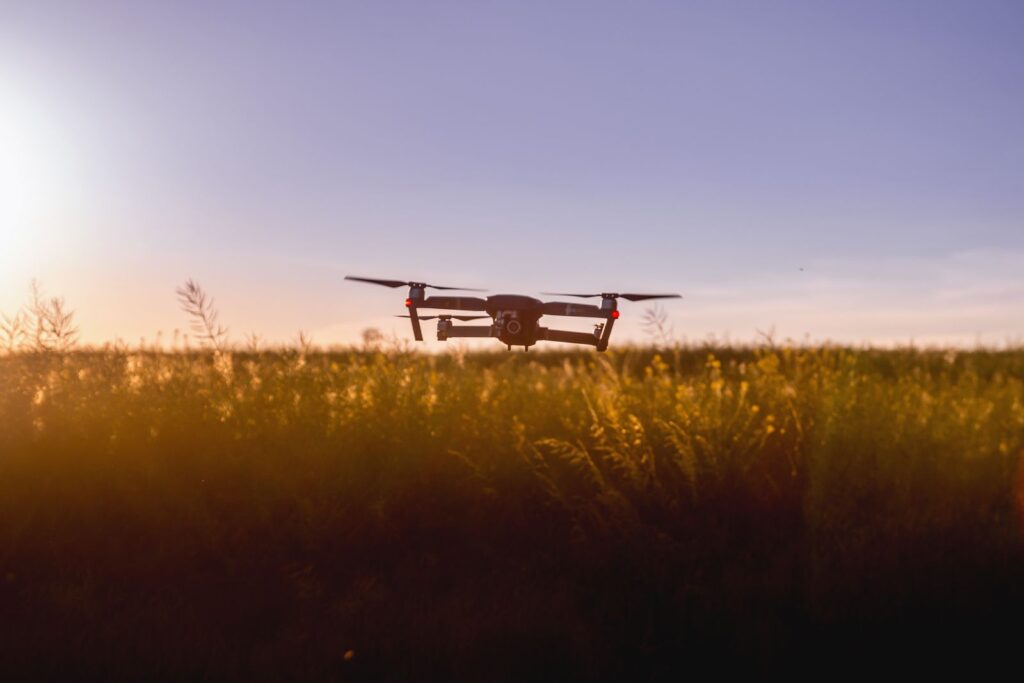 A drone flying over a field of tall grass against a violet evening sky