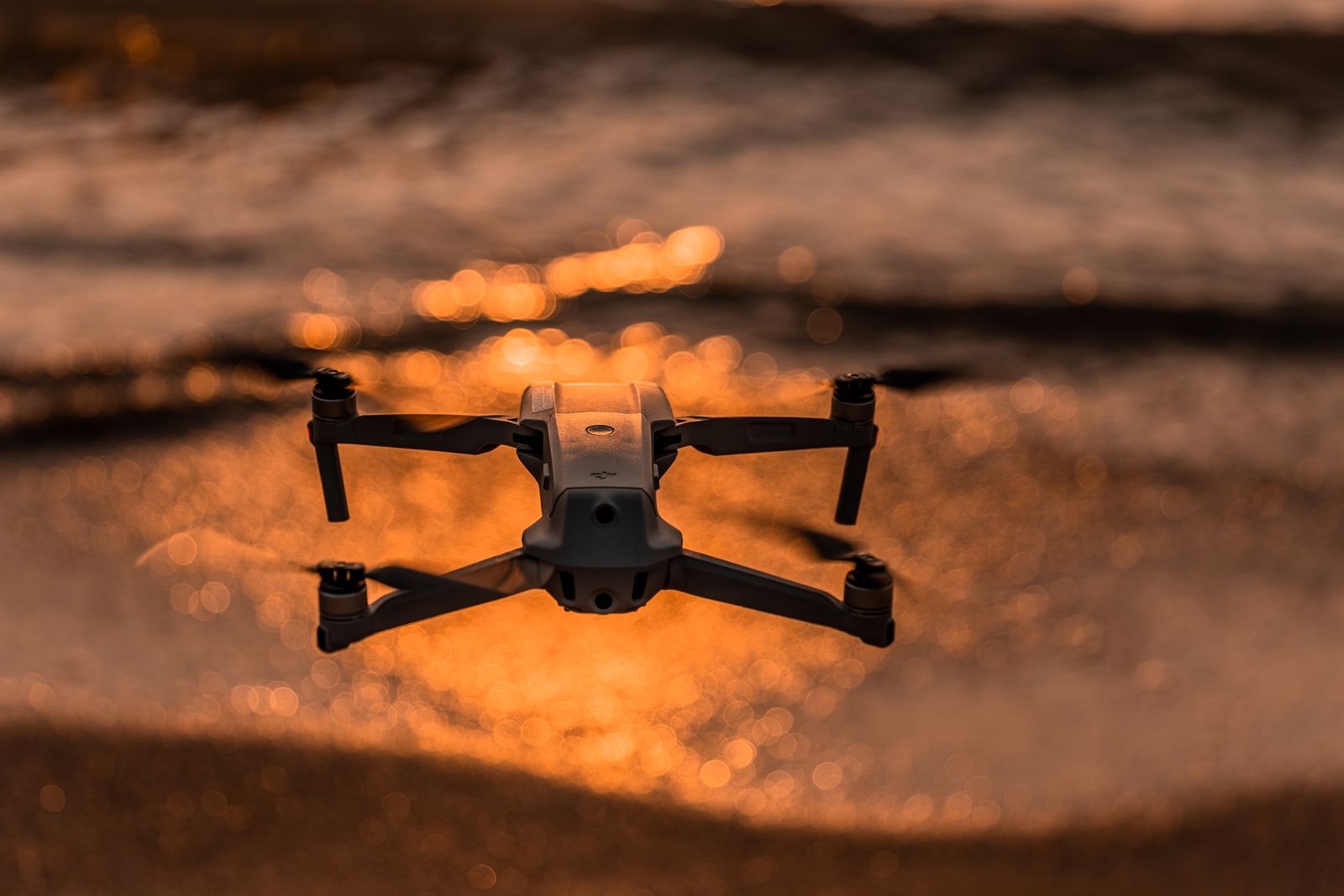 A folding drone flying low over water that glows orange at sunset