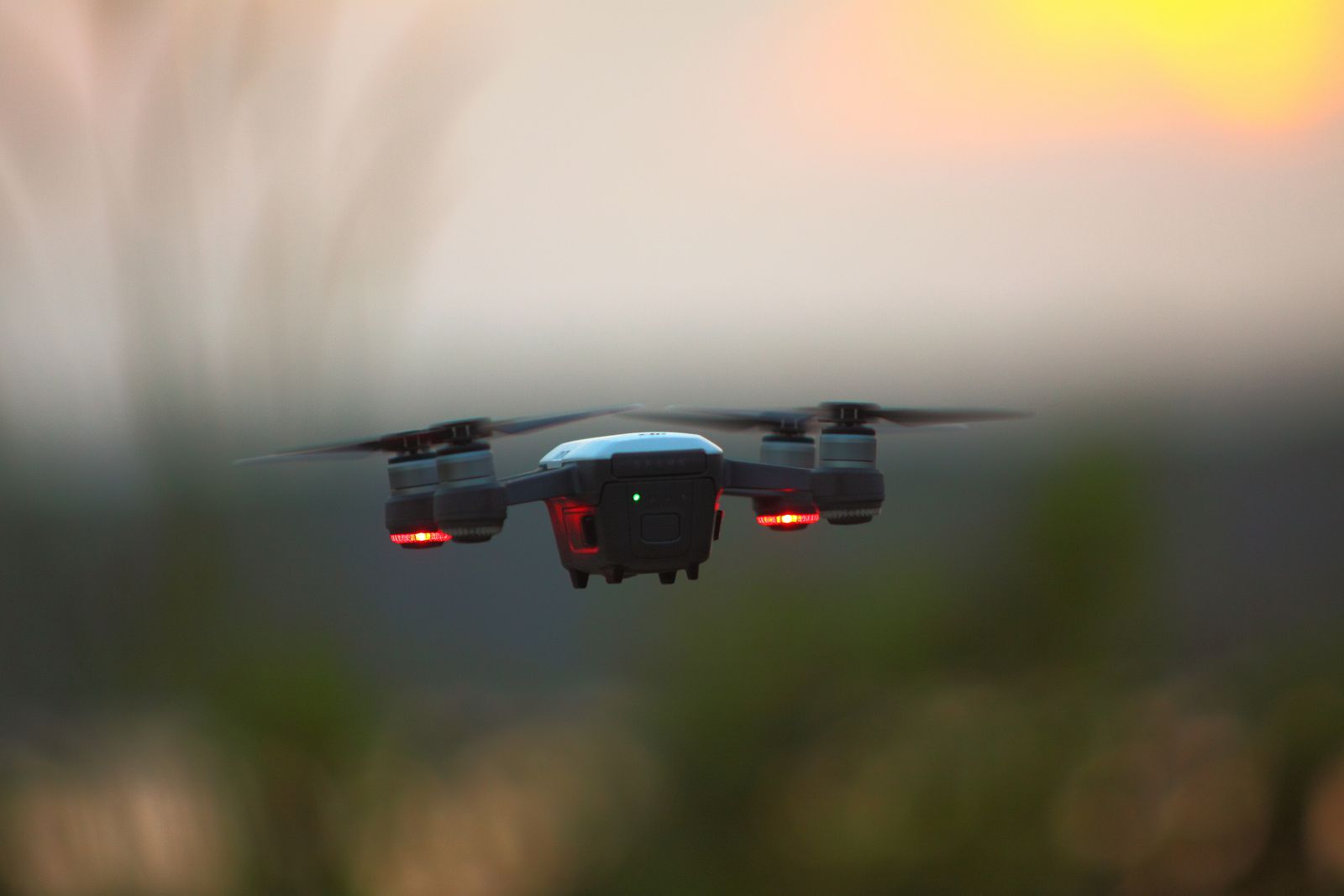 A small drone hovering at sunset with its red lights on