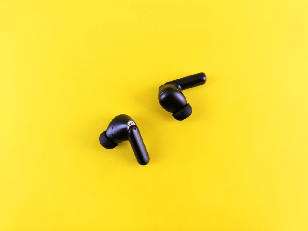Two black wireless earbuds on a bright yellow background