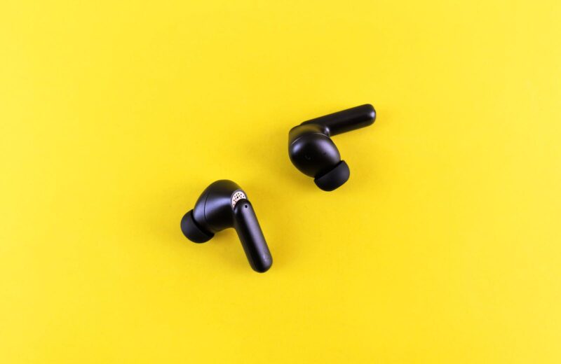 Two black wireless earbuds on a bright yellow background