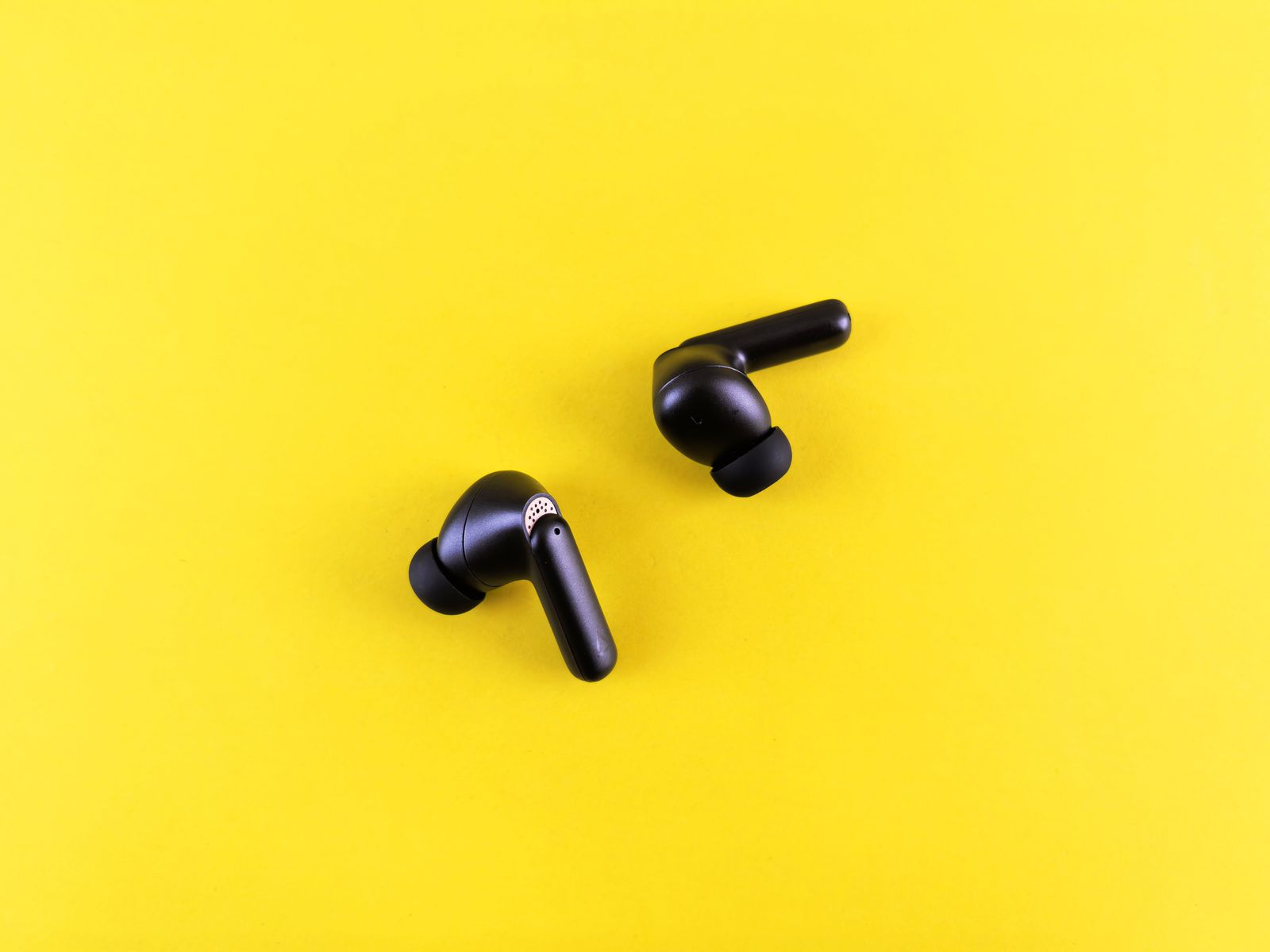 Two black wireless earbuds on a bright yellow background