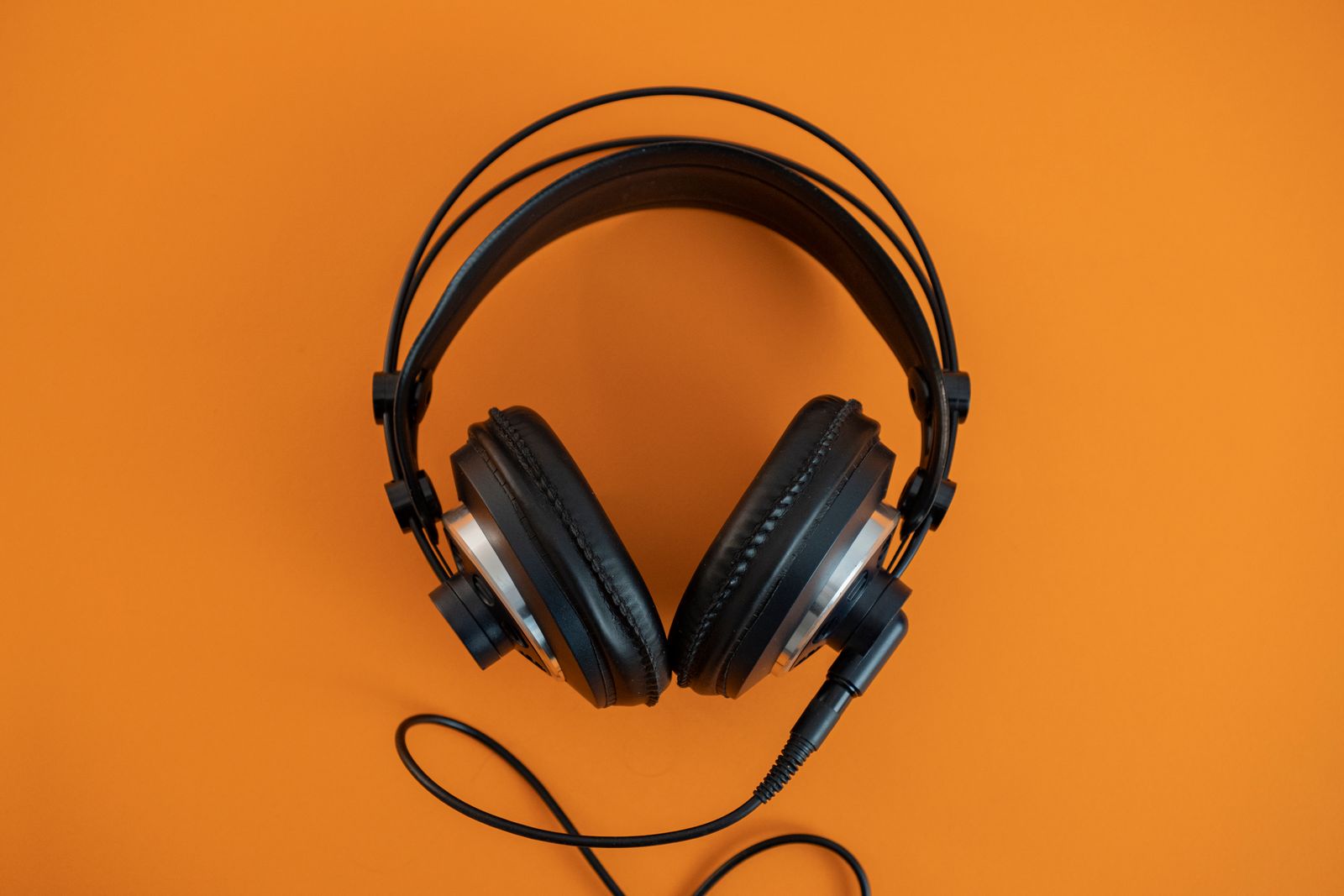 Black studio headphones with a coiled cable on a bright orange background