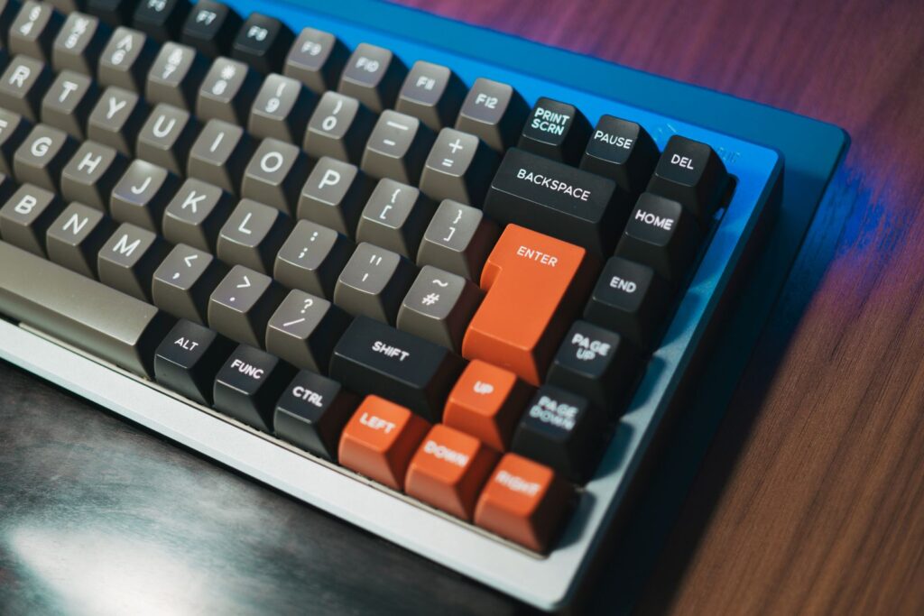 A mechanical keyboard with grey and black keycaps and orange arrow keys on a wooden desk