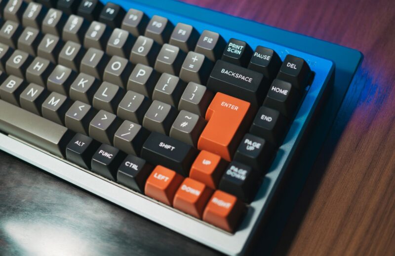 A mechanical keyboard with grey and black keycaps and orange arrow keys on a wooden desk
