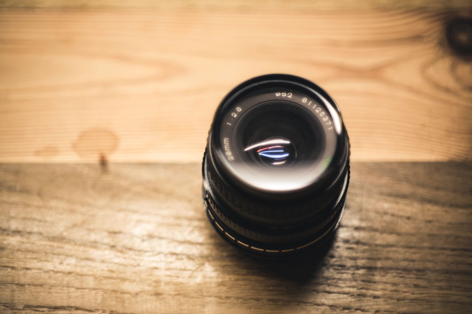 A small camera lens standing on a wooden table in warm light