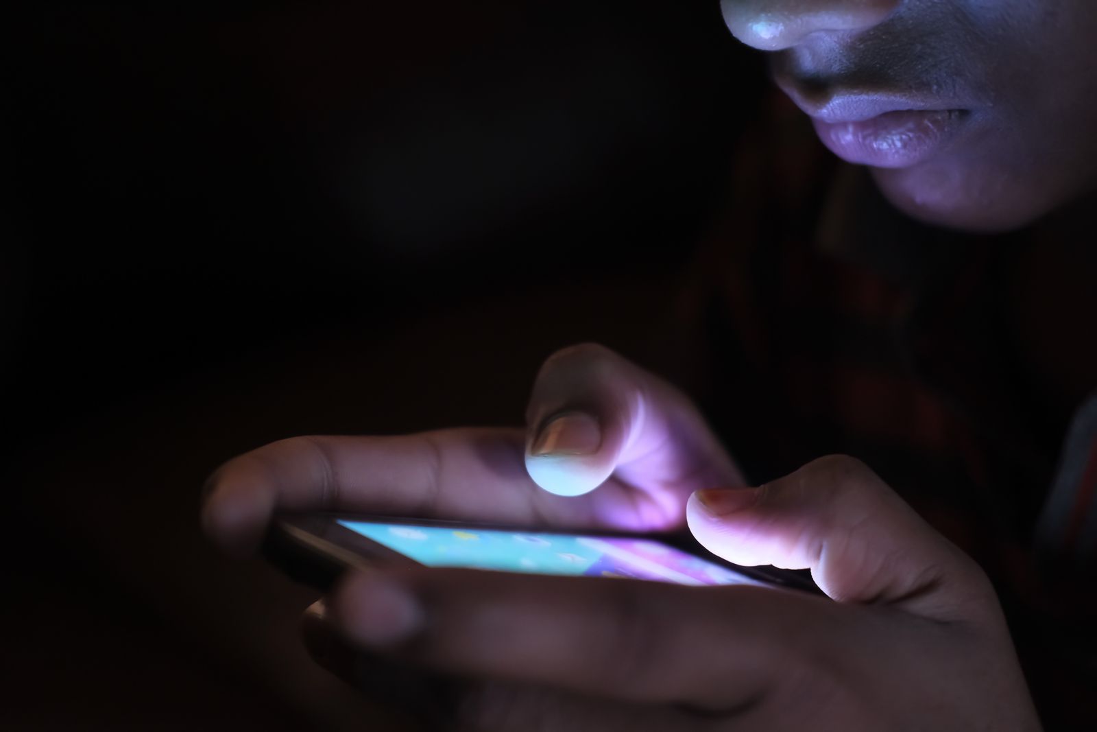 Two hands holding a smartphone in the dark, the screen lighting the fingers
