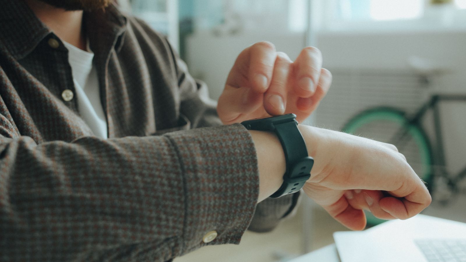 A person in a checked shirt tapping a smartwatch with a black strap on the wrist