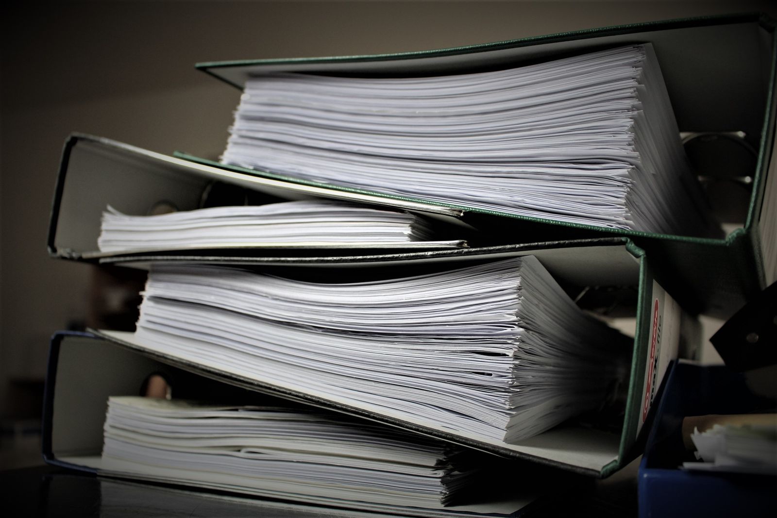 A stack of thick ring binders full of paper on an office shelf