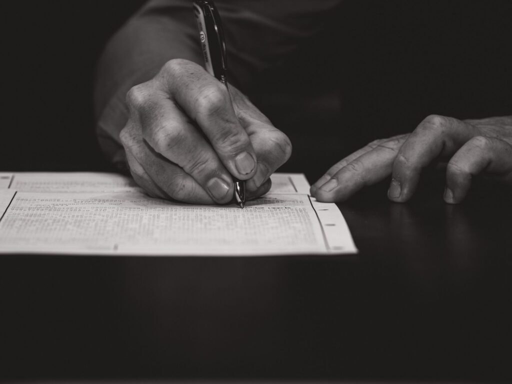 A hand signing a printed form with a pen, in black and white