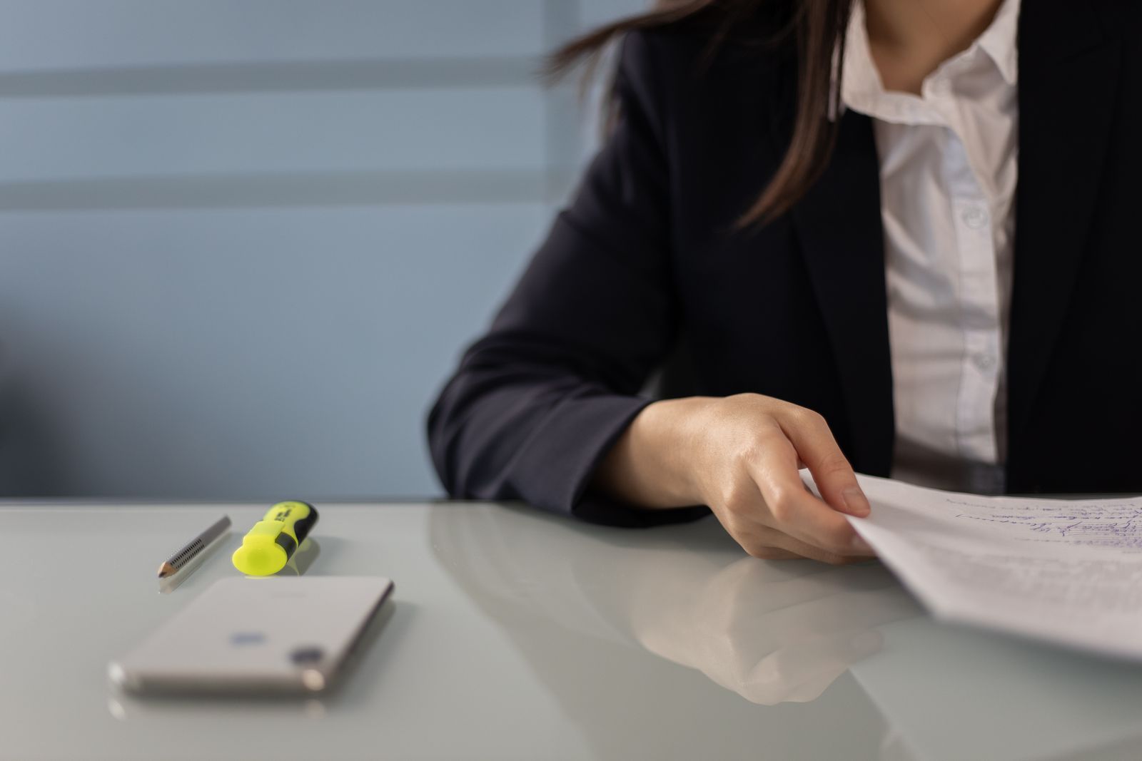 A person in a dark jacket reading a printed document at a grey desk