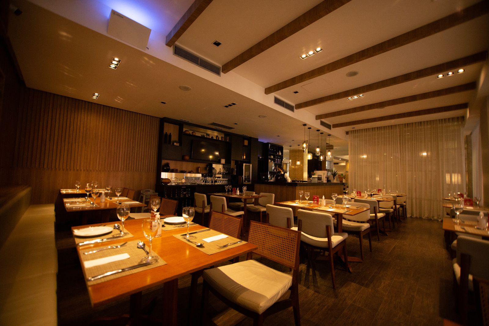 Restaurant dining room laid for evening service with wooden tables and warm lights