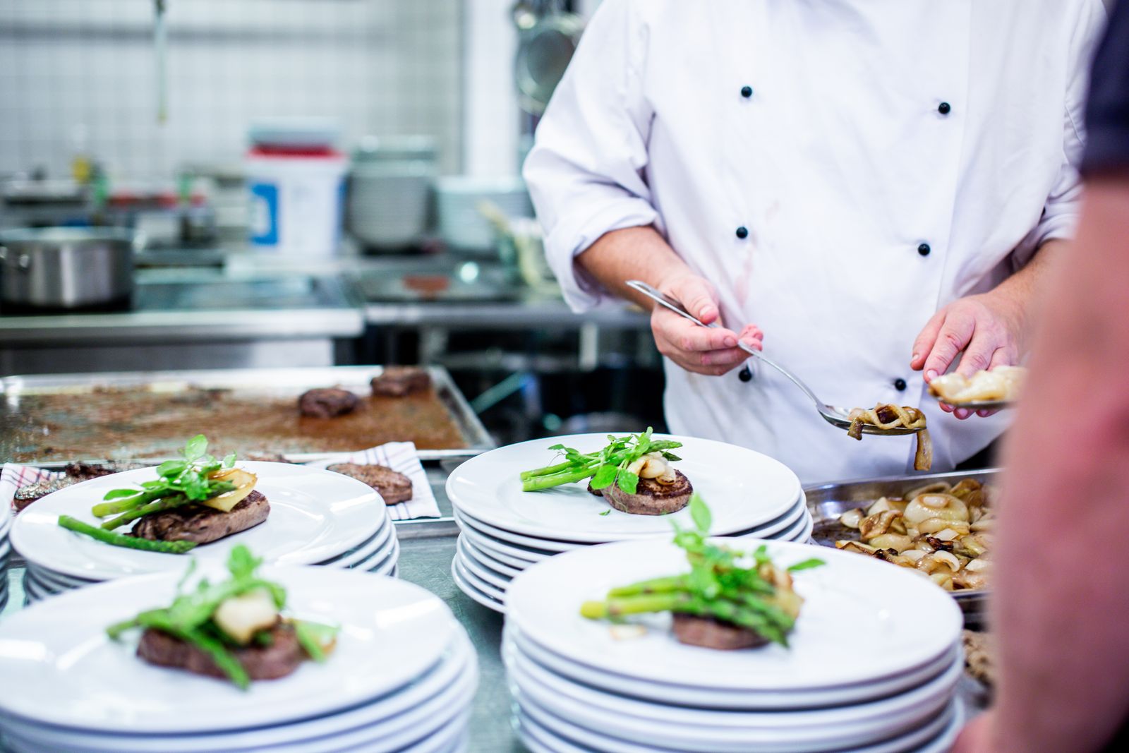 A cook finishing a row of plates with green beans and sauce