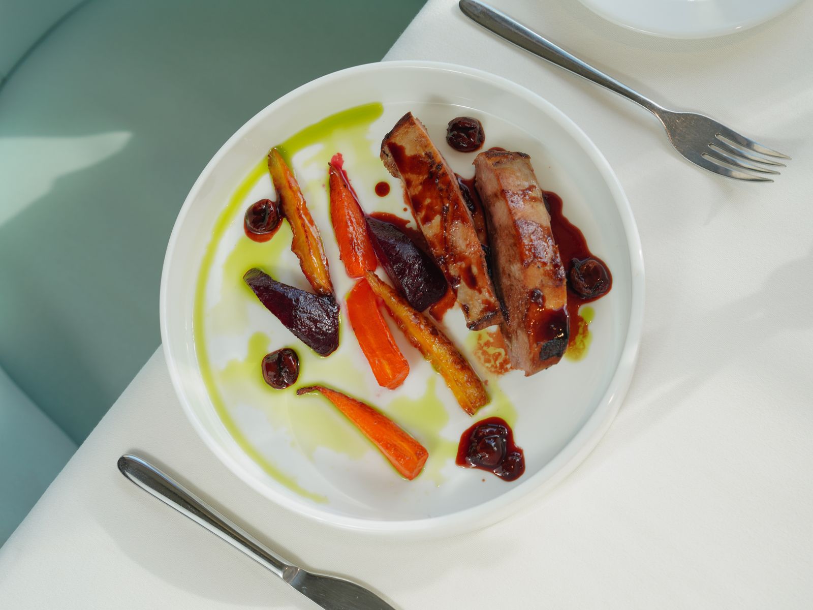 Glazed meat with roasted carrots and beetroot on a white plate, seen from above