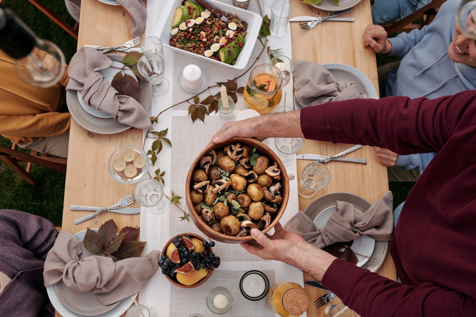 A shared table seen from above with roast dishes and hands passing plates