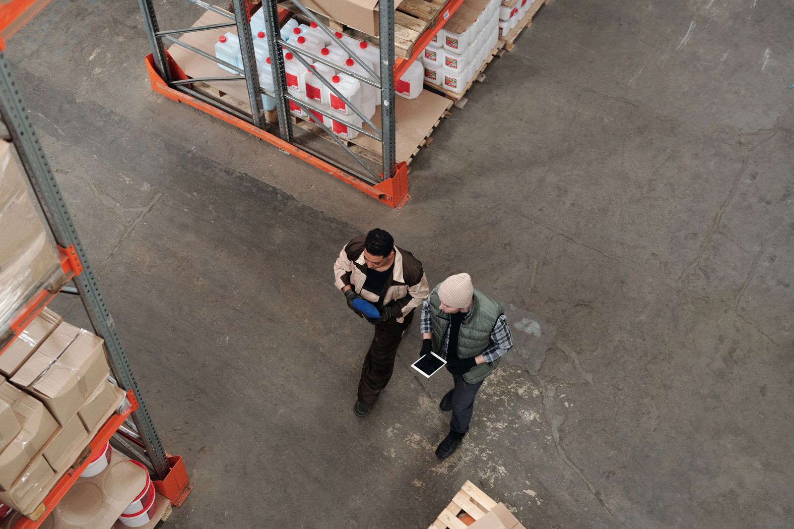 Two warehouse workers seen from above walking between racks, one holding a tablet