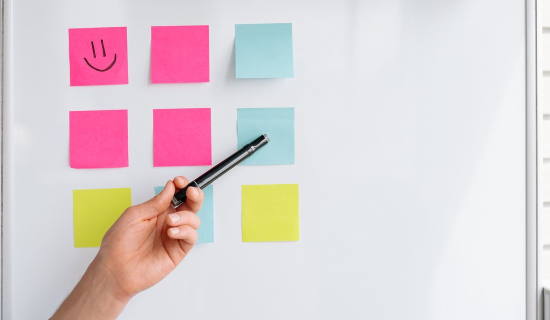 A hand pointing a marker at rows of sticky notes on a planning board