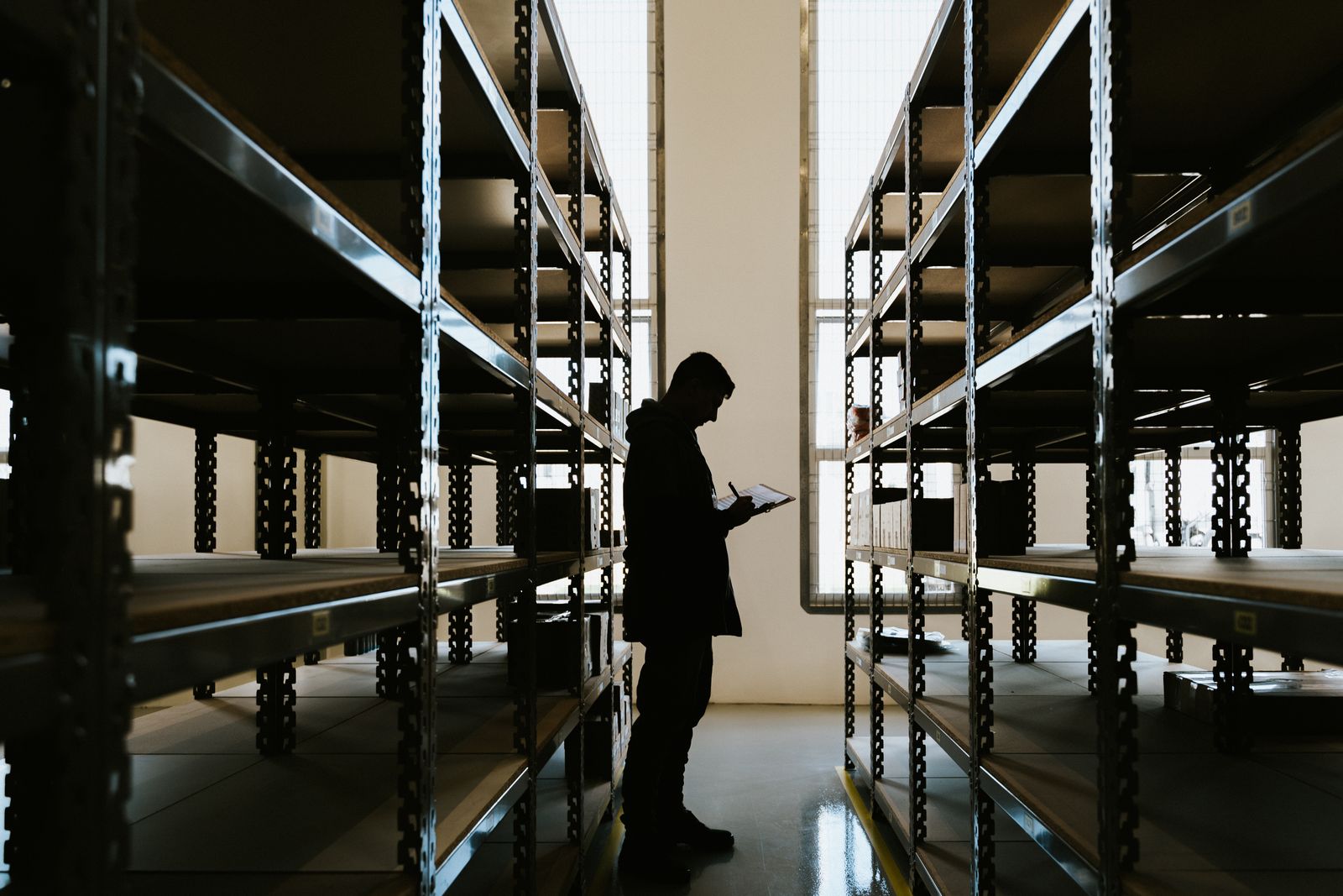 Silhouette of a person with a clipboard standing between tall warehouse shelves (sample portrait)