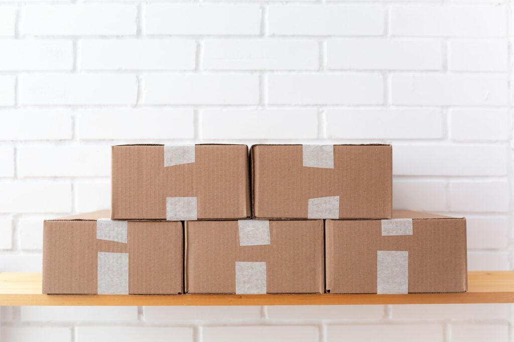 Taped cardboard boxes stacked on a shelf against a white brick wall
