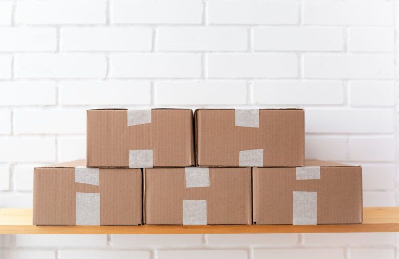 Taped cardboard boxes stacked on a shelf against a white brick wall