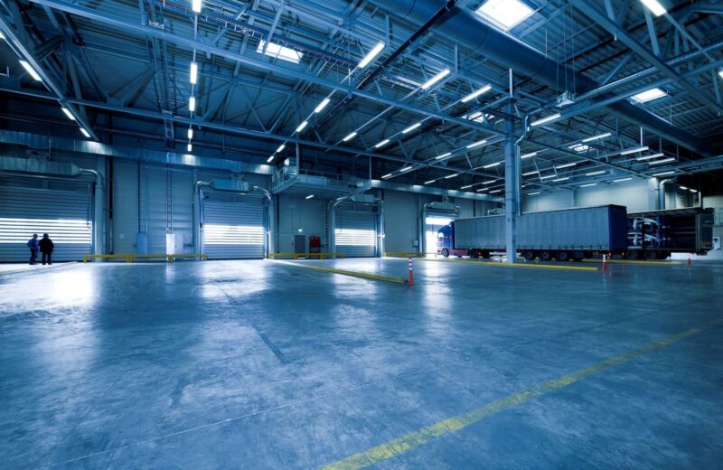 An empty, brightly lit loading hall with roller doors and one trailer at the far end