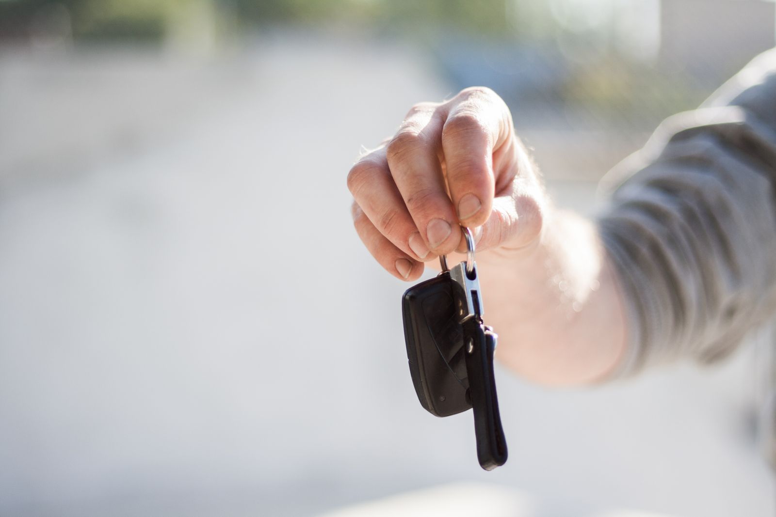 A hand holding out a car key against a soft, blurred background