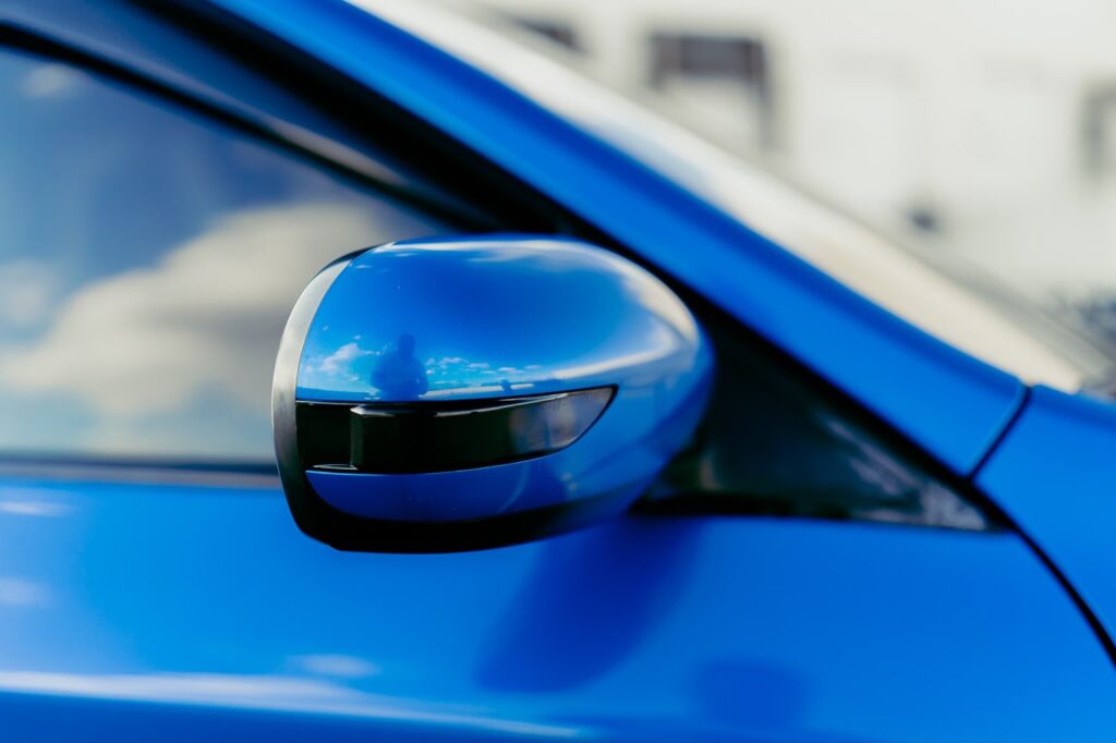 The side mirror of a blue car reflecting the sky