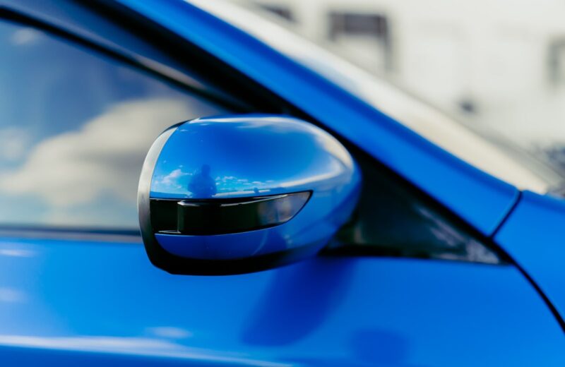 The side mirror of a blue car reflecting the sky