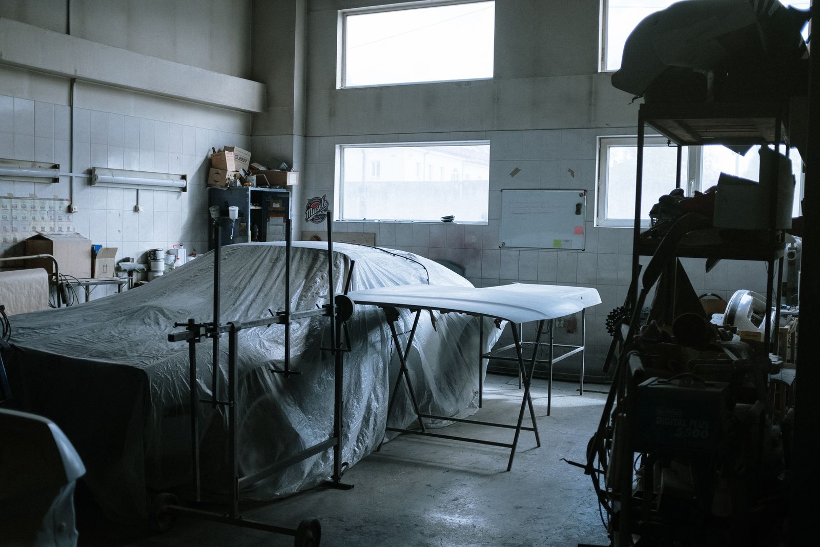 A covered car in a preparation workshop with tools and lamps around it