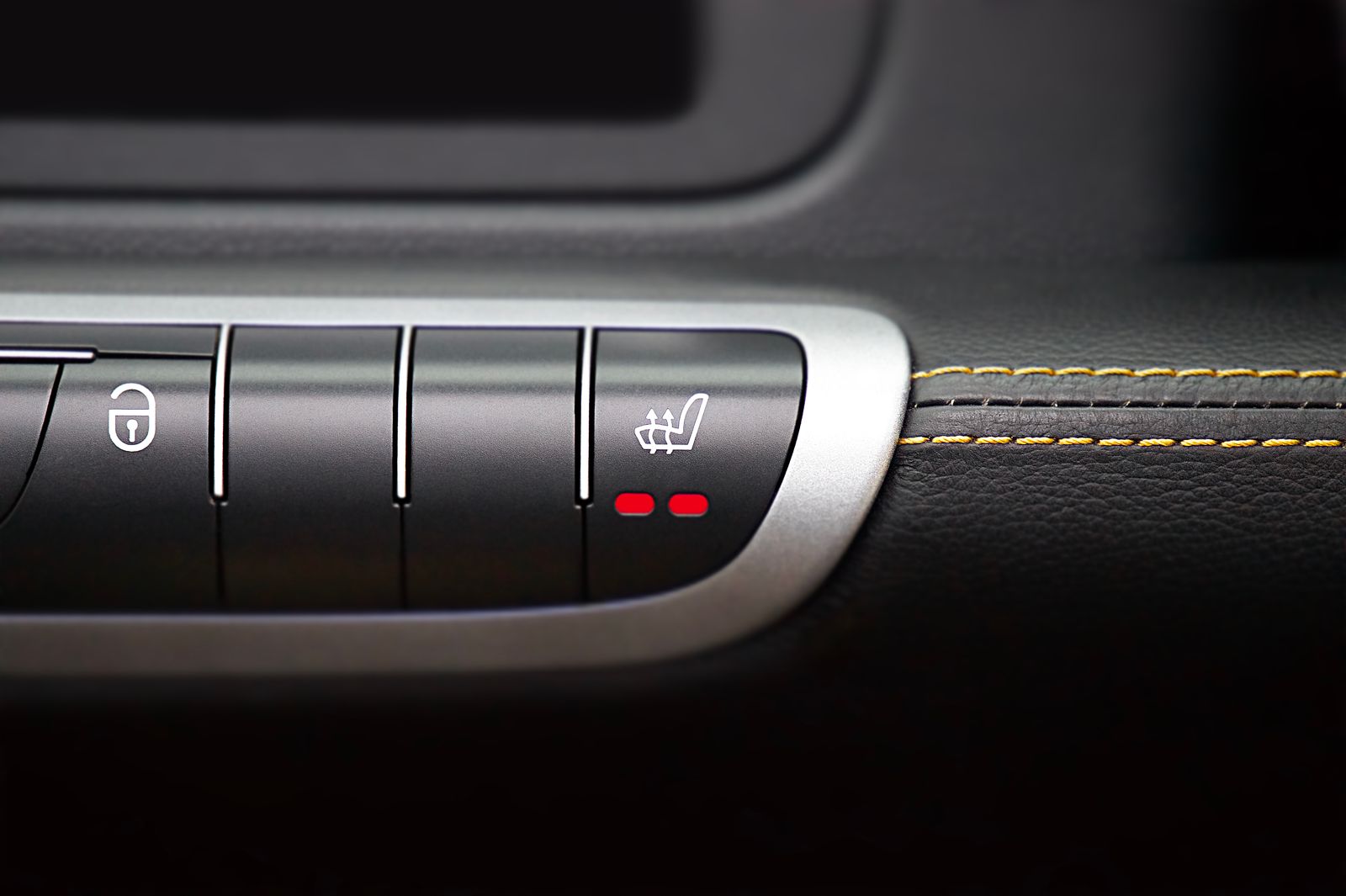 Close-up of a car console with seat-heating buttons and pale contrast stitching on black leather