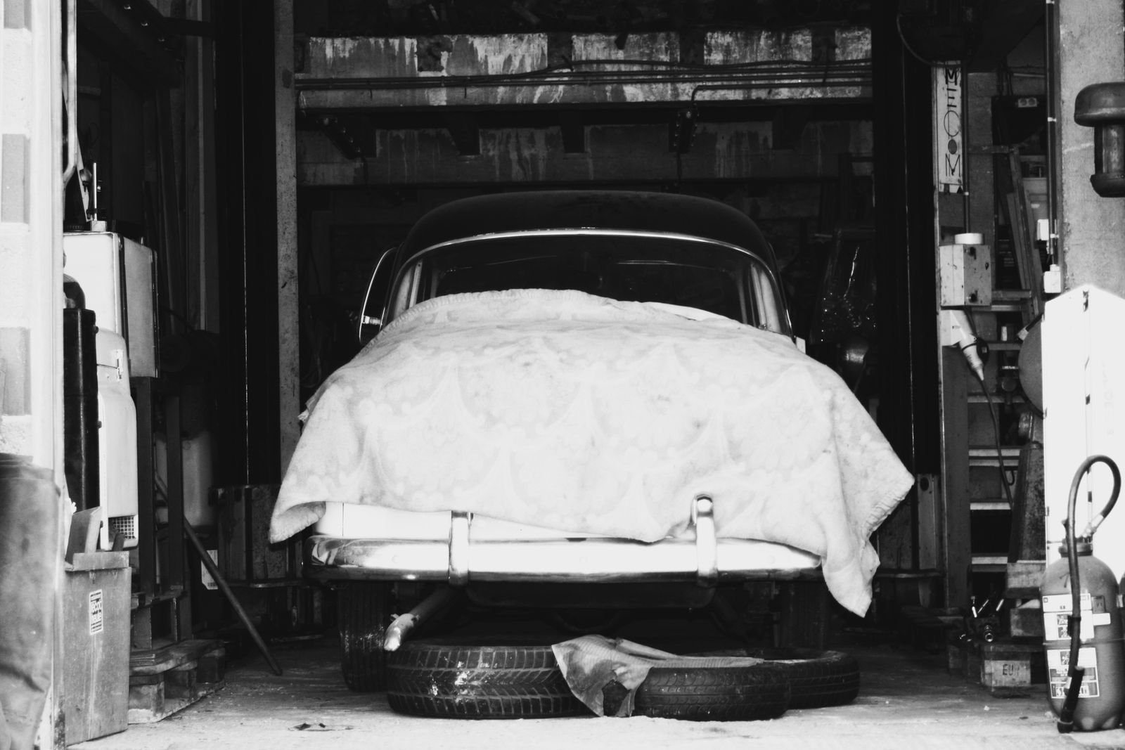 Black and white photo of a classic car under a fitted cover in a garage