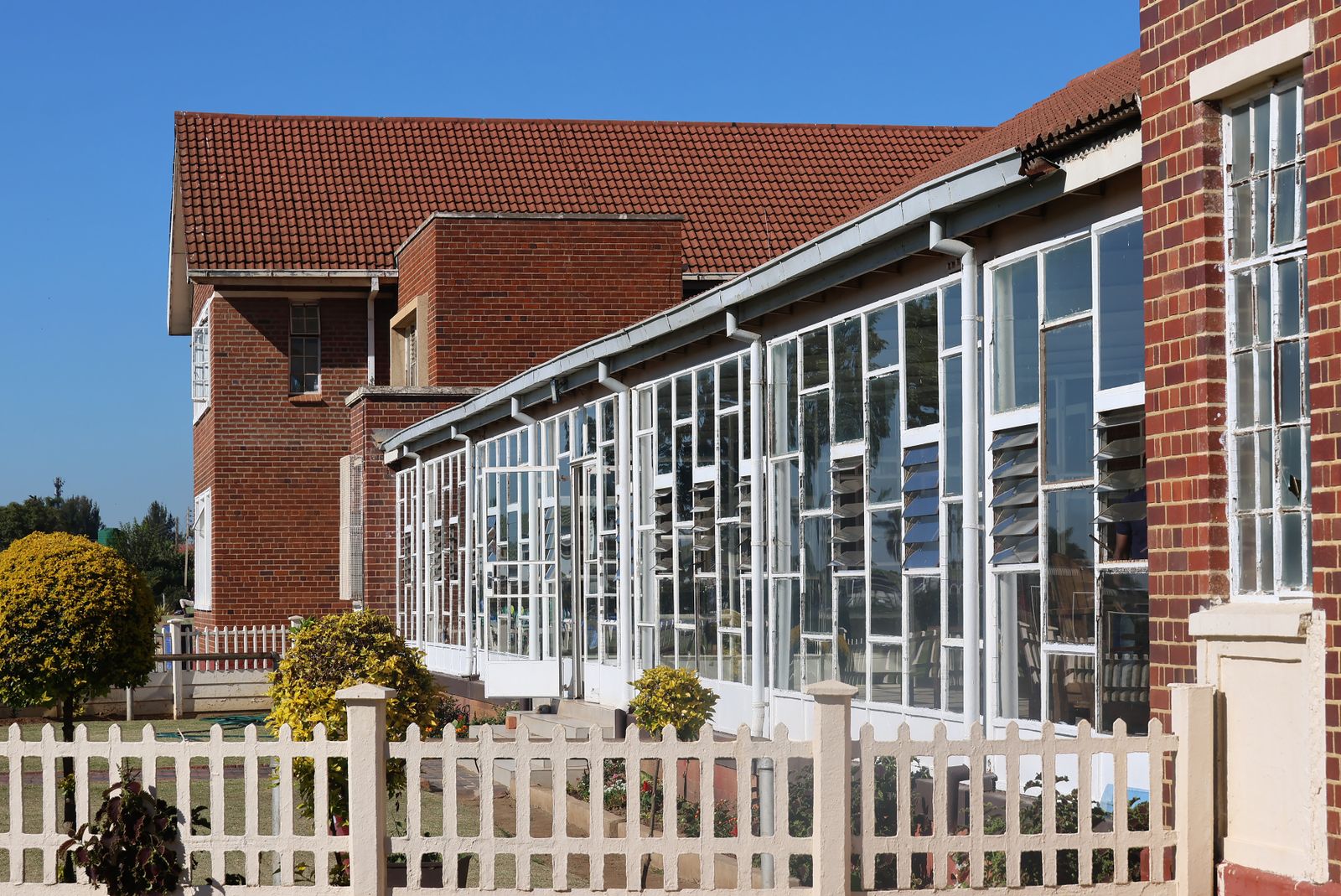 Brick school building with tall glass windows and a red roof