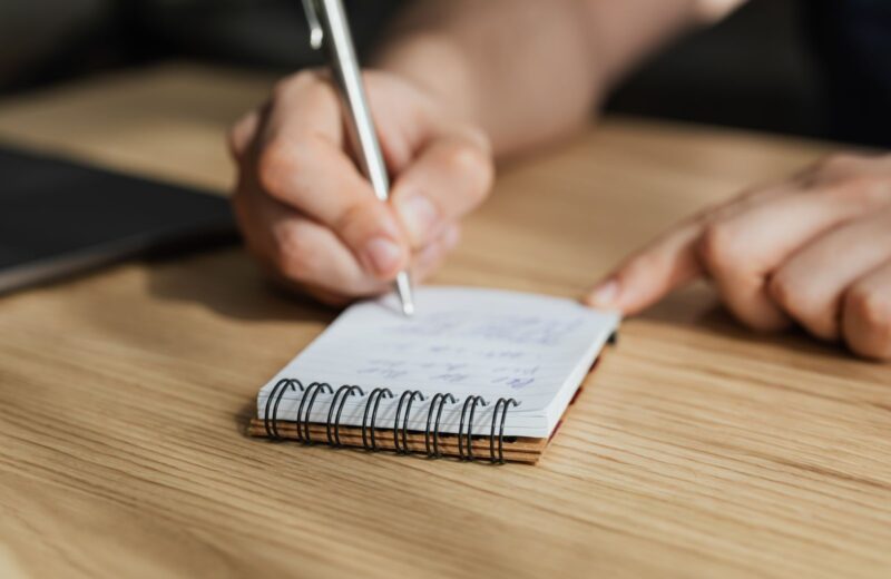 A student writing in a notebook at a wooden desk