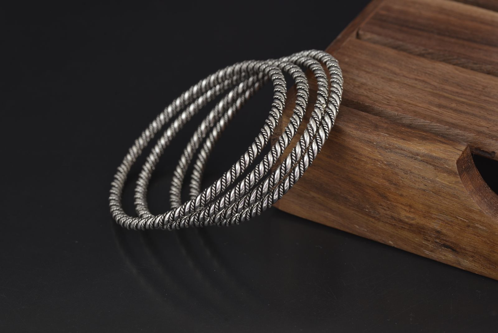 Three twisted silver bangles resting on the edge of a dark wooden board